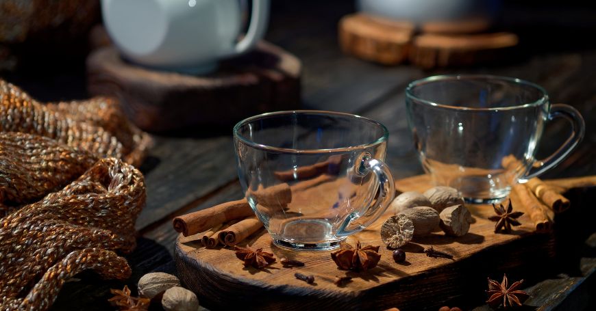 two empty cups with a chai latte teapot in the background